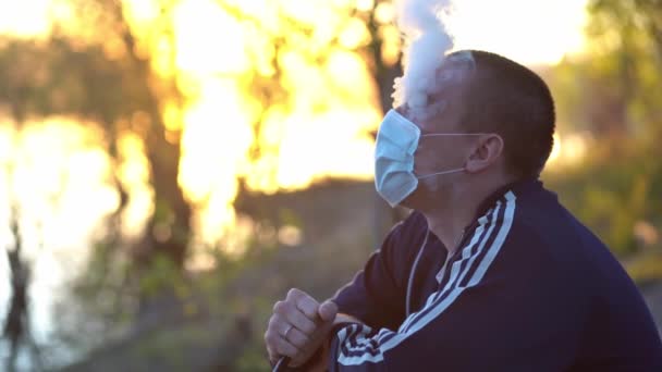 Adam yüzünde tıbbi maskenin altındaki dumanı salıyor. — Stok video