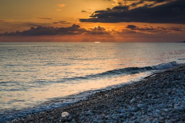 küçük bir dalga üzerinde batan güneşin altında bir çakıl plajı