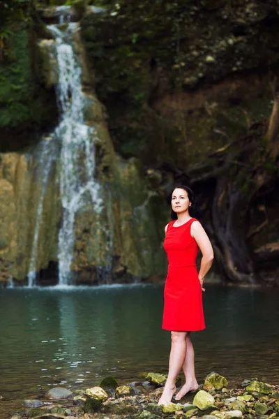 一个穿红色裙子的黑发女孩的肖像在瀑布 — 图库照片