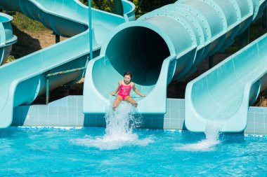 küçük bir kız pembe bir mayo slayt aşağı aqua parka alır.