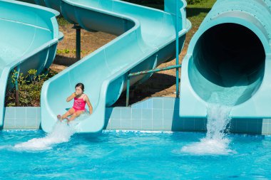 küçük bir kız pembe bir mayo slayt aşağı aqua parka alır.