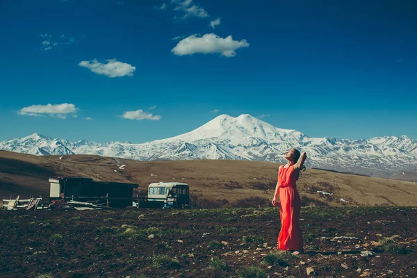brunette slim girl with closed eyes in long red dress on the background of high snow-capped mountains