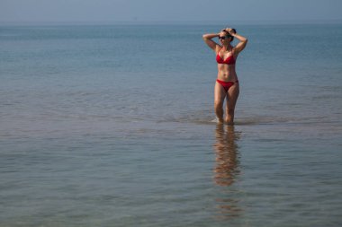 Kırmızı bikinili ince kız deniz güneş gözlüğü ile sığ suda duruyor