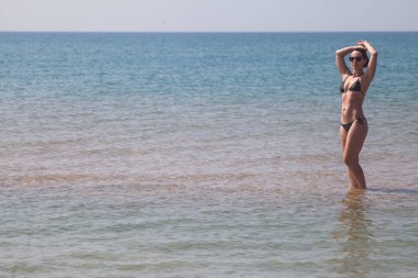 güzel bir rakam siyah bikini ve deniz ayak bileği-derin kumlu bir balık suda ayakta güneş gözlüğü ile esmer kız