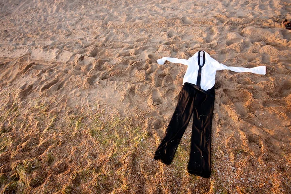 wet clothes black pants and white shirt lying on the sand