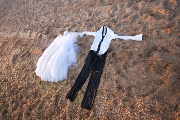 wet clothes black pants and white shirt lie next to the wedding dress on the sand