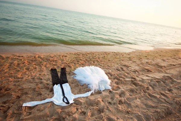 wet clothes black pants and white shirt lie next to the wedding dress on the sandy beach