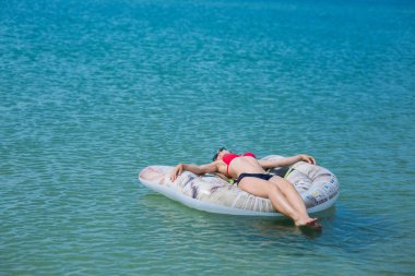 Kırmızı bikinili Avrupalı ince kız güneş gözlüğü ile şişme bir şilte üzerinde okyanusta yüzüyor