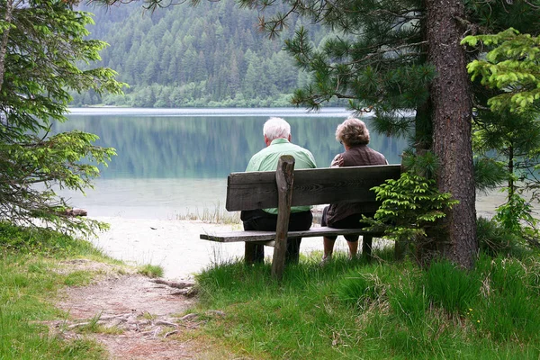 Пожилая пара, сидящая на скамейке у озера — стоковое фото