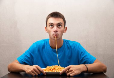 Domates soslu spagetti yiyen genç bir adam.