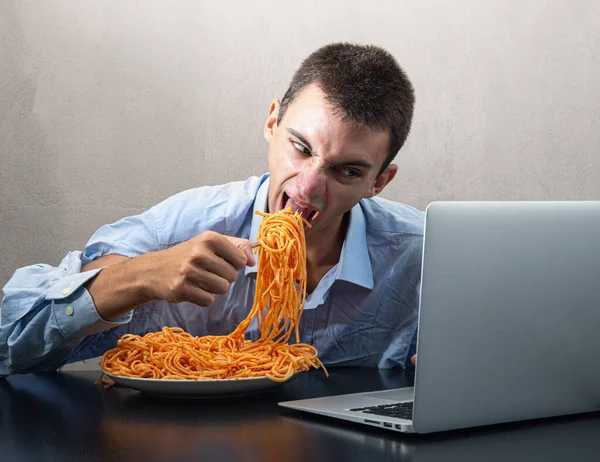 Domates soslu spagetti yiyen ve bilgisayar izleyen bir adam.