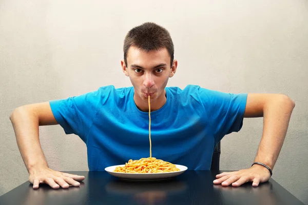 Domates soslu spagetti yiyen genç bir adam.