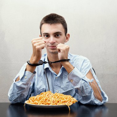 Elleri kelepçeli spagetti yiyen genç bir adam.