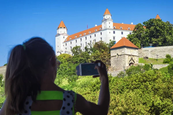 A girl is taking pictures of a white castle in Bratislava. Castle Bratislava. White Castle in Bratislava.Medieval castle on the hill against the sky, Bratislava, Slovakia.