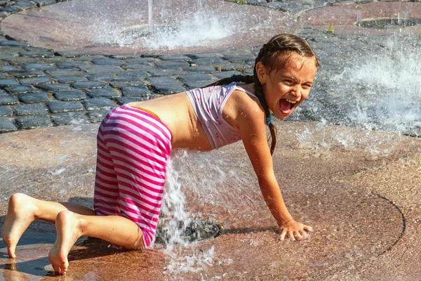 Girl on a sunny summer day are poured water from a fountain.Girl happily in shallow clean water on of city fountain on warm bright summer day.