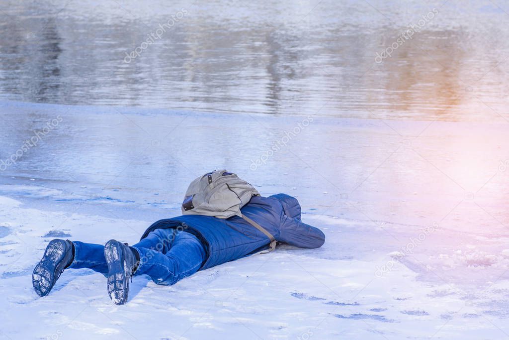 The man lies on ice in the winter,a man lies on the ice of the winter river and looks through the ice .
