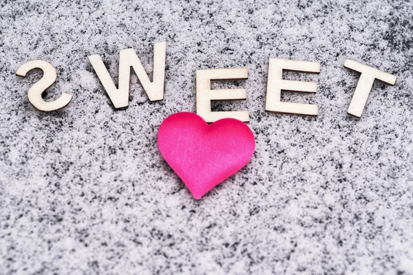 Heart drawn in the snow.Valentine\'s Day. Heart of pink in the snow with the letters sweet. Valentine\'s Day. Soft focus. Background. Close-up
