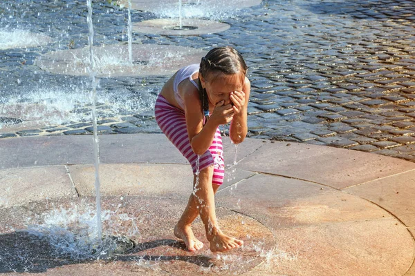 Girl on a sunny summer day are poured water from a fountain.Girl happily in shallow clean water on of city fountain on warm bright summer day.