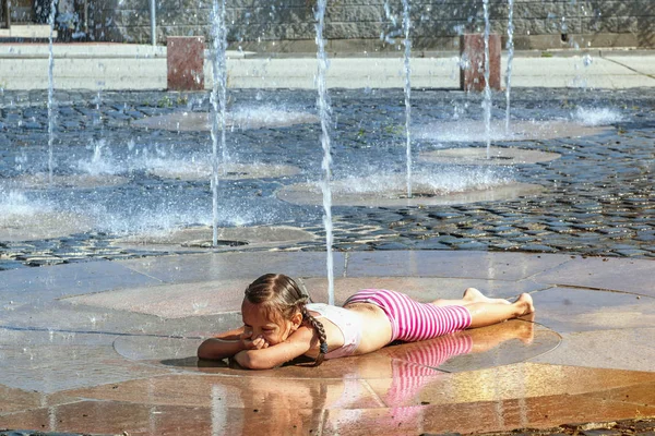 Girl on a sunny summer day are poured water from a fountain.Girl happily in shallow clean water on of city fountain on warm bright summer day.