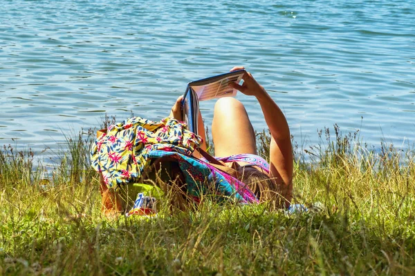 A girl lies in a river and reads a book. Young woman reading a book sitting by the river.