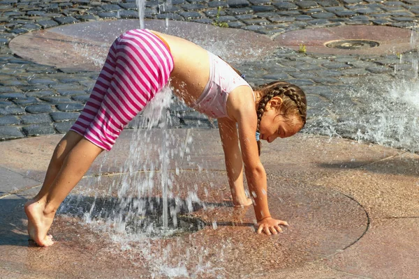 Girl on a sunny summer day are poured water from a fountain.Girl happily in shallow clean water on of city fountain on warm bright summer day.
