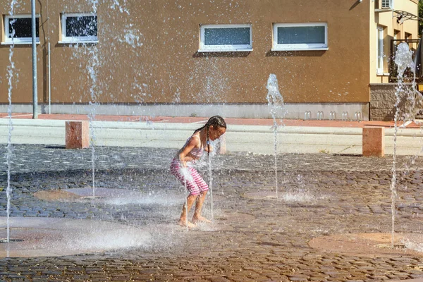 Meisje op een zonnige warme dag buiten spelen in een waterfontein. Meisje gelukkig in ondiepe schoon water op van stad fontein op warme heldere zomerdag. — Stockfoto