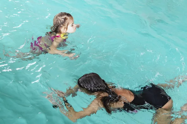 Twee meisjes zwemmen in het zwembad. Twee zussen in het zwembad. Twee gelukkige meisjes spelen in het zwembad. Mooie meisjes zwemmen en plezier in het water. Actieve vakantie. — Stockfoto