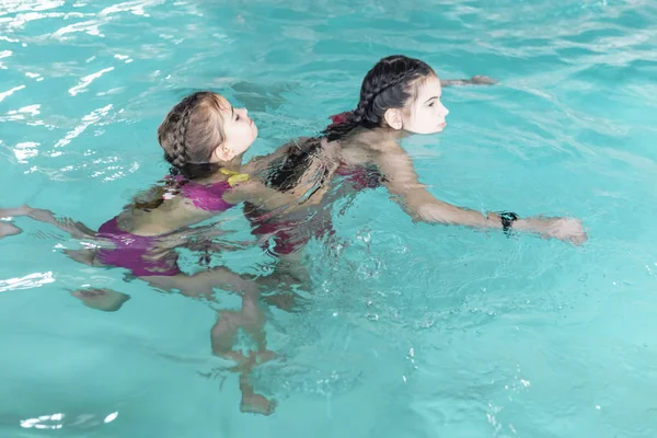 Twee meisjes zwemmen in het zwembad. Twee zussen in het zwembad. Twee gelukkige meisjes spelen in het zwembad. Mooie meisjes zwemmen en plezier in het water. Actieve vakantie. — Stockfoto