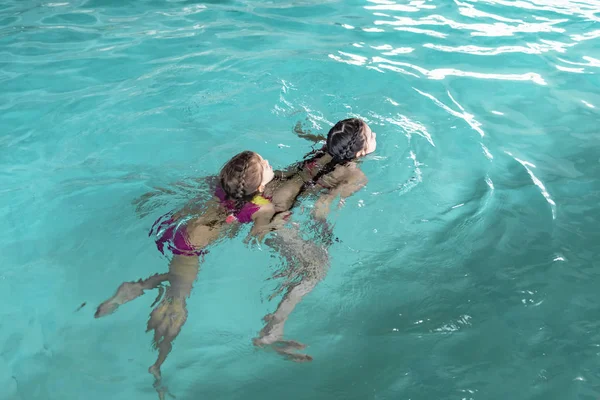 Twee meisjes zwemmen in het zwembad. Twee zussen in het zwembad. Twee gelukkige meisjes spelen in het zwembad. Mooie meisjes zwemmen en plezier in het water. Actieve vakantie. — Stockfoto