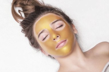 Güzel kız kozmetik maskesi yüzünde altın rengi. Yakın çekim. Boş alan. Kadın altın maske. Güzel model altın yüz cilt kozmetik kaldırma. Güzellik Cilt Bakımı .