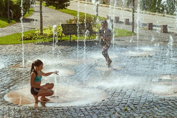 Kinderen op een zonnige warme dag buiten spelen in een waterfontein. Kinderen gelukkig in ondiep schoon water op de stad fontein op warme lichte zomerdag. — Stockfoto