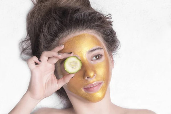 Hermosa chica con una máscara cosmética en la cara de color dorado. Primer plano. Espacio libre. Máscara de oro mujer. Hermoso modelo de eliminación de cosméticos de piel facial dorada. Cuidado de la piel de belleza  . — Foto de Stock