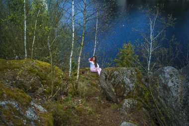 Bir kız bir uçurumun üzerinde oturur ve doğaya bakar, kız bir kaya üzerinde oturan ve vadi manzarasının keyfini.