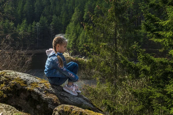 Een meisje zit op een klif en kijkt naar de natuur, meisje zittend op een rots en genieten van het uitzicht op de vallei. — Stockfoto