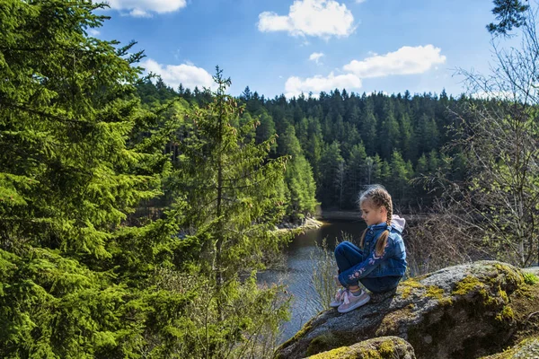 Een meisje zit op een klif en kijkt naar de natuur, meisje zittend op een rots en genieten van het uitzicht op de vallei. — Stockfoto