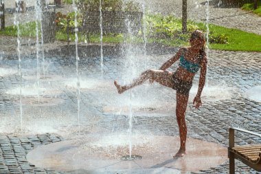 Güneşli sıcak bir günde bir su çeşmesi dışında oynarken kız. Gı