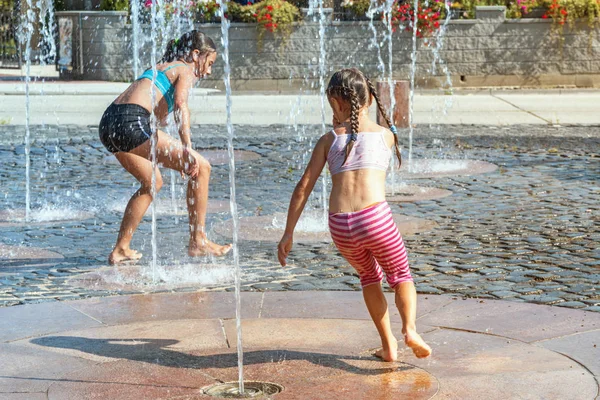 Kinderen op een zonnige warme dag buiten spelen in een waterfontein. Kinderen gelukkig in ondiep schoon water op de stad fontein op warme lichte zomerdag. — Stockfoto