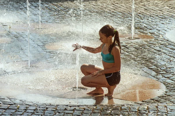 Pige på en solrig varm dag leger udenfor i et vand springvand. Gi - Stock-foto