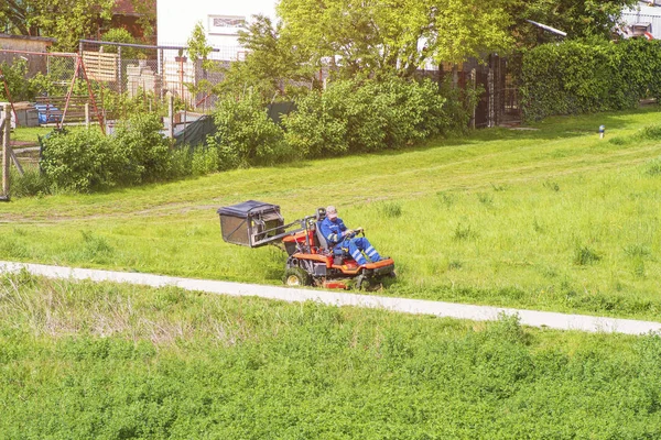 Uomo maturo che guida erba taglierina in un sole dGardener guida un tosaerba equitazione in un giardino.Operaio falciatura erba nel parco cittadino. Giornata estiva soleggiata . — Foto Stock