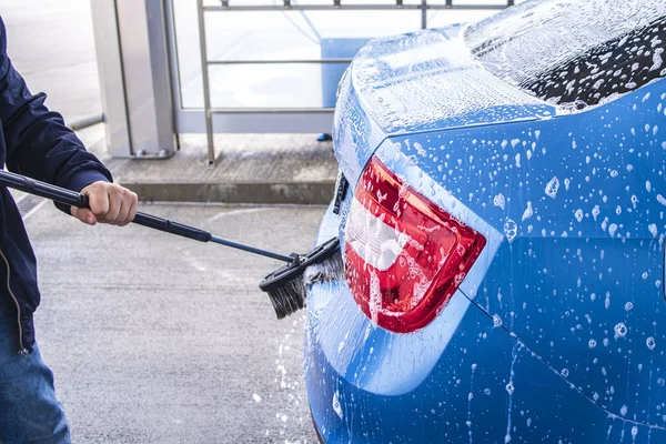 Using a brush to wash a car on a car washing facility on sunny summer day.Manual car wash with pressurized water in car wash outside.Blue car manual wash of with pressurized water in car wash outside. — Stock Photo, Image