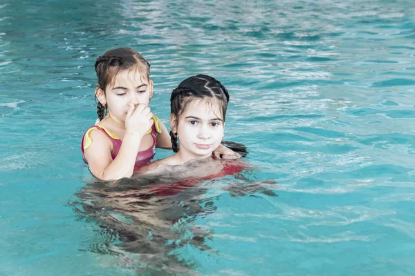 Twee meisjes zwemmen in het zwembad. Twee zussen in het zwembad. Twee gelukkige meisjes spelen in het zwembad. Mooie meisjes zwemmen en plezier in het water. Actieve vakantie. — Stockfoto