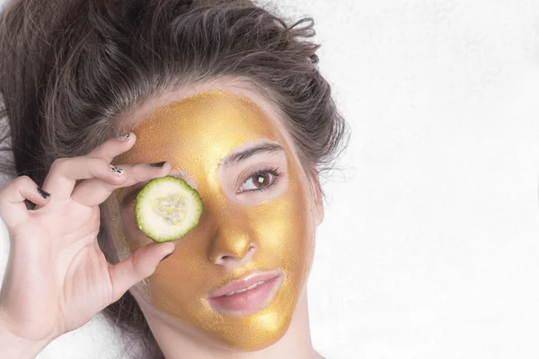 Hermosa chica con una máscara cosmética en la cara de color dorado. Primer plano. Espacio libre. Máscara de oro mujer. Hermoso modelo de eliminación de cosméticos de piel facial dorada. Cuidado de la piel de belleza  . — Foto de Stock