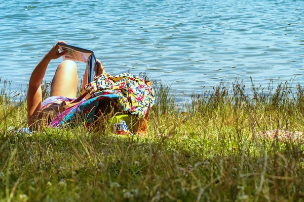 Een meisje ligt in een rivier en leest een boek. Jonge vrouw het lezen van een boek terwijl zittend bij de rivier. — Stockfoto