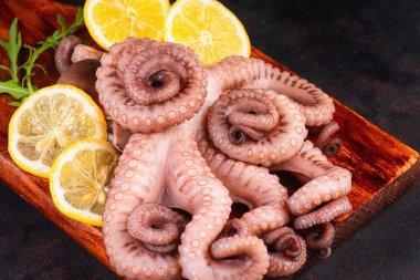 Deniz ürünleri. Ahşap mutfak tahtasına çiğ ahtapot dokunaçları ve limon dilimleri..