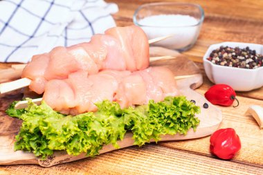 Taze tavuk kebabı. Baharatlı, yeşil marullu, kırmızı biberli ve soğanlı mutfak tahtasındaki çiğ tavuk şişleri..