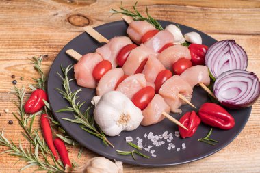 Taze tavuk kebabı. Siyah tabakta çiğ tavuk şişi. Baharatlar, yeşil biberiye, kırmızı biber ve ahşap zemin üzerinde soğan. Şişte çiğ tavuk şişi..