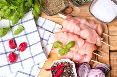 Taze tavuk kebabı. Baharat ve yeşil fesleğen yapraklı mutfak tahtasındaki çiğ tavuk şişleri. Kırmızı acı biber ve soğan..