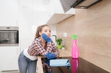 Yorgun genç bir temizlikçi evi temizledikten sonra mutfakta dinlenir, mutfak tezgahına yaslanır. Genç bir kız düşünceli bir şekilde koruyucu eldivenlerle mutfakta durur..
