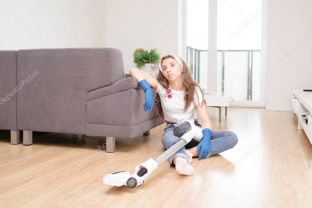 woman using vacuum cleaner in the living room.Young girl cleans the apartment. Tired girl after cleaning sits on the floor with a vacuum cleaner.
