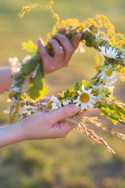 Midsummer in Latvia: celebration of Ligo - a young woman weave a wreath and collect field flowers